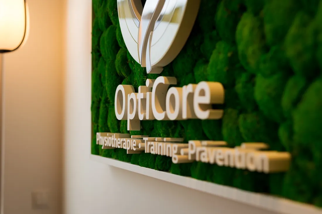 OptiCore-Wandschild auf grüner Mooswand – Physiotherapie, Training und Prävention in Heidelberg